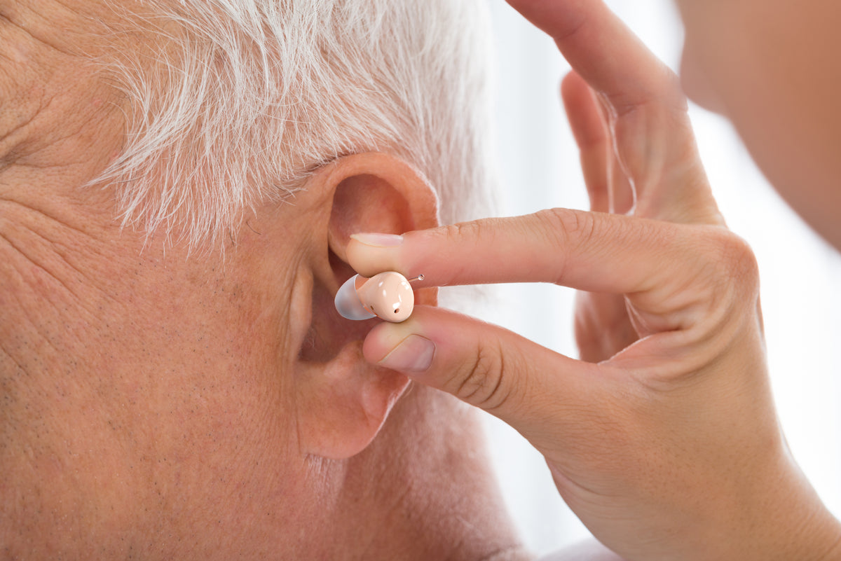 Person adjusting a hearing aid in an elderly person's ear.