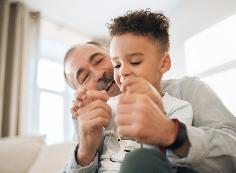 Grandfather and young grandson laughing together on a sofa at home