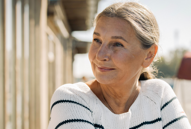 Older woman in a striped sweater outdoors, smiling as she looks into the distance