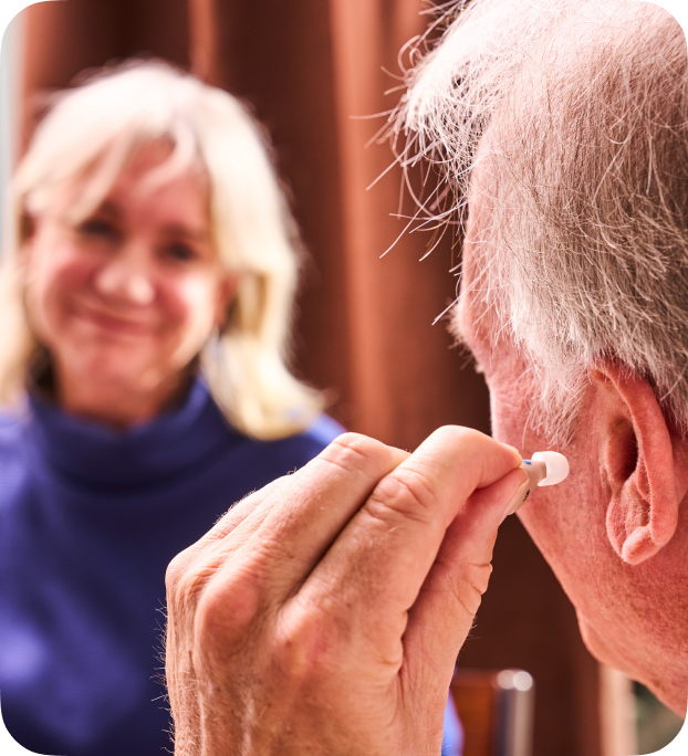 Adult placing a discreet hearing aid in the ear at home