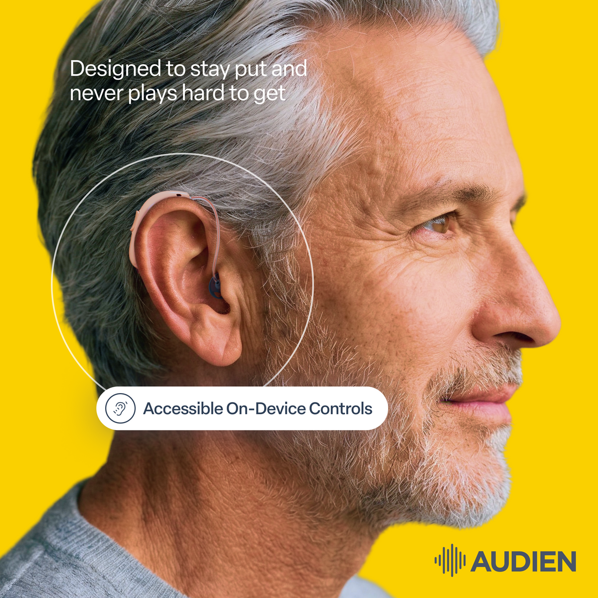 A close-up side profile of a man with gray hair and beard wearing a small behind-the-ear hearing device. White text reads 'Designed to stay put and never plays hard to get' above the ear, and a label below says 'Accessible On-Device Controls.