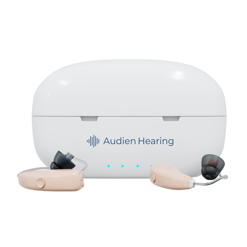 Audien hearing aids placed in front of closed charging case with blue indicator lights

